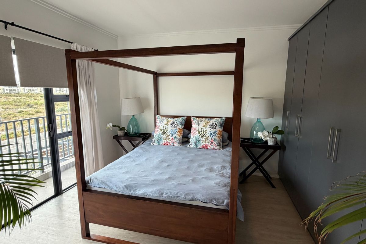 A well-maintained bedroom featuring modern built-in cupboards, laminate flooring, and a large sliding glass door providing access to a balcony.