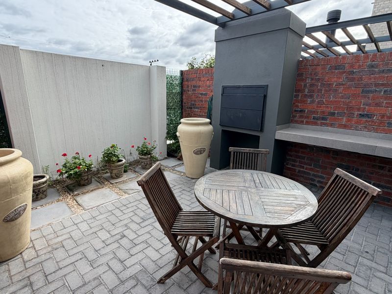 Outdoor patio area featuring a built-in braai, concrete counter, and pergola structure, finished with paved flooring and brick wall accents.