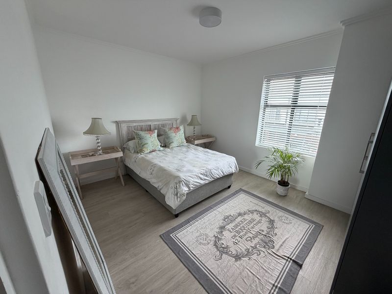 A bright and well-maintained bedroom featuring light-toned laminate flooring, neutral walls, and venetian blinds for adjustable natural light.