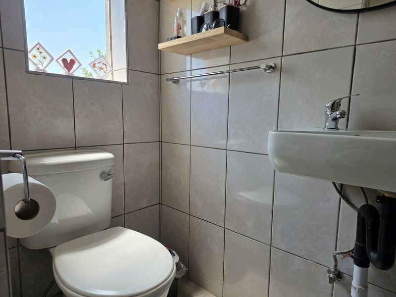 A compact, tiled bathroom featuring a wall-mounted basin with a chrome mixer tap and a standard toilet.