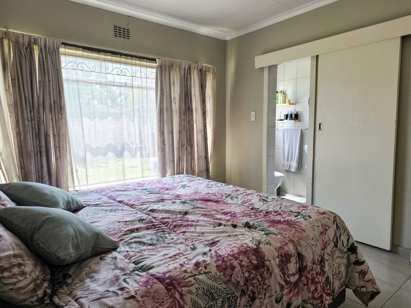 A bedroom featuring a window with security bars and a sliding door providing access to an en-suite bathroom.