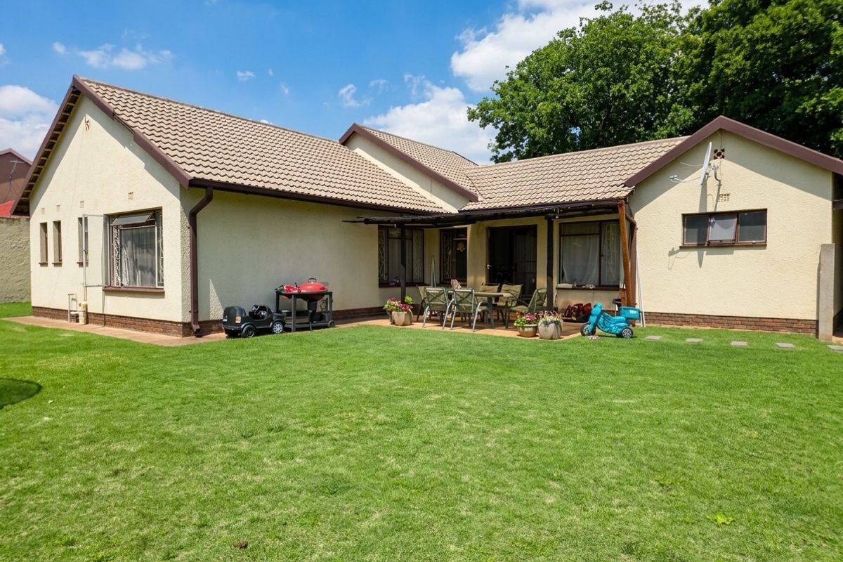 Rear view of the house featuring a covered patio area, paved terrace, and a well-maintained lawn.