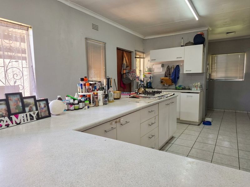 Functional kitchen featuring white built-in cabinetry, laminate countertops, a gas hob, and ceramic floor tiles, offering a practical layout for daily meal preparation.
