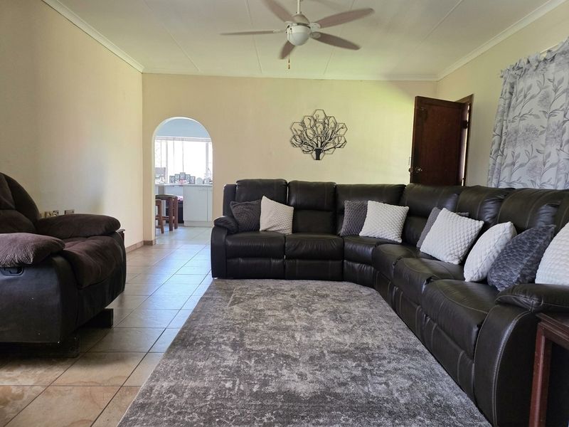 A spacious living room featuring tiled flooring, a ceiling fan, and an arched entryway leading to an adjacent kitchen area.