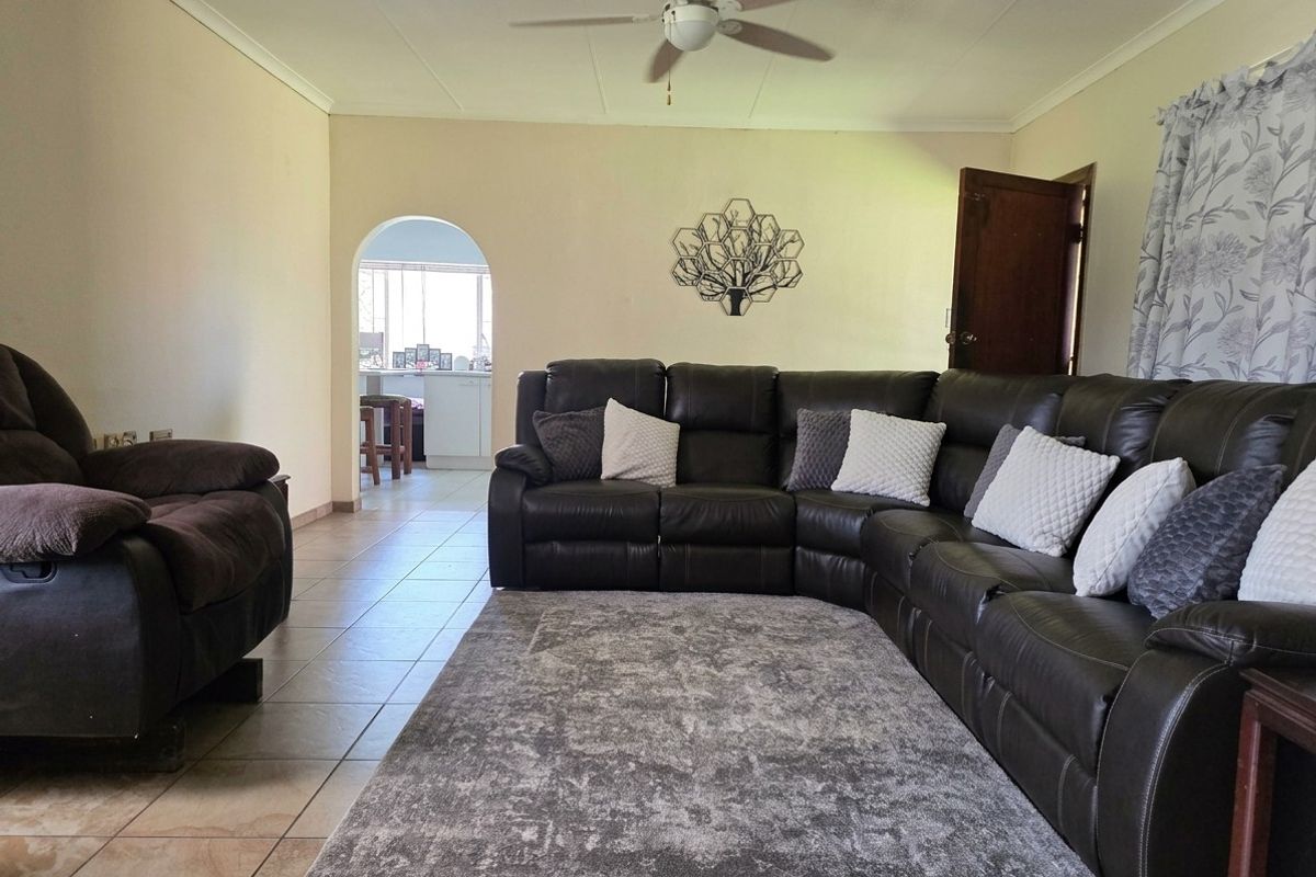 A spacious living room featuring tiled flooring, a ceiling fan, and an arched entryway leading to an adjacent kitchen area.