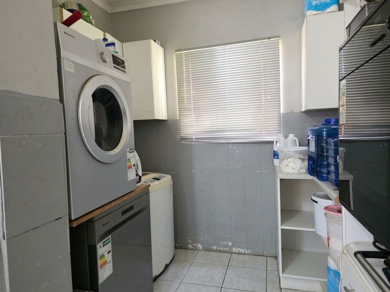 A functional laundry room featuring tiled flooring, built-in cabinetry, and wall tiling, showing signs of wear on the lower wall surfaces.