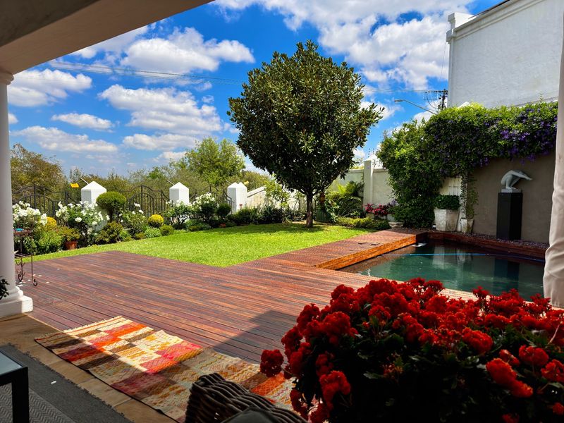 A well-maintained outdoor pool area featuring timber decking, a swimming pool, and a landscaped garden with established trees and boundary fencing.
