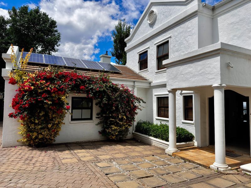 A well-maintained front entrance featuring a paved courtyard, classic architectural columns, and roof-mounted solar panels on a white rendered facade.