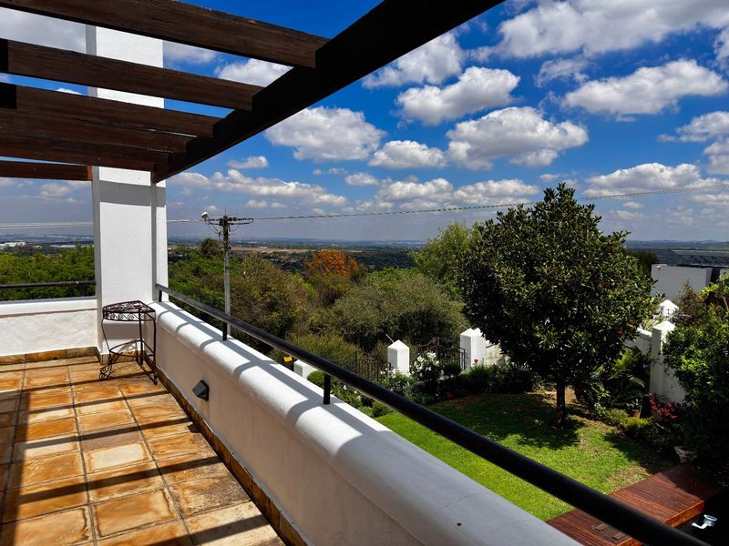 A spacious covered balcony featuring a timber pergola, tiled flooring, and a metal balustrade, offering elevated views over the garden and surrounding landscape.
