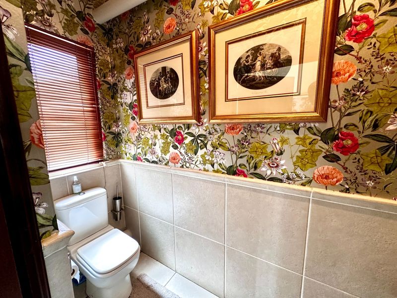 A compact powder room featuring floral wallpaper, half-height wall tiling, and a standard toilet suite with window blinds.
