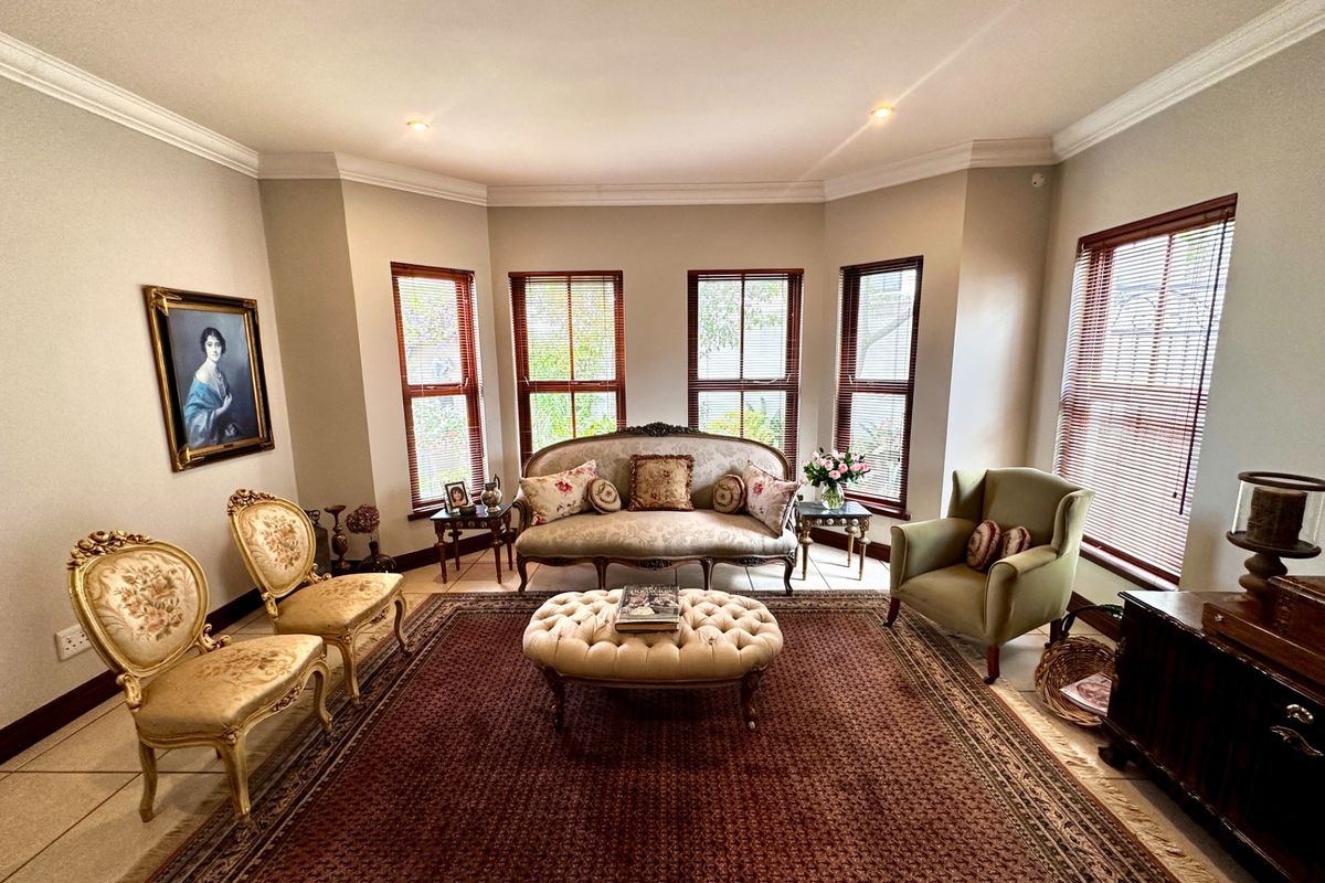 A well-maintained living room featuring a large bay window with venetian blinds, crown molding, recessed lighting, and neutral tiled flooring.