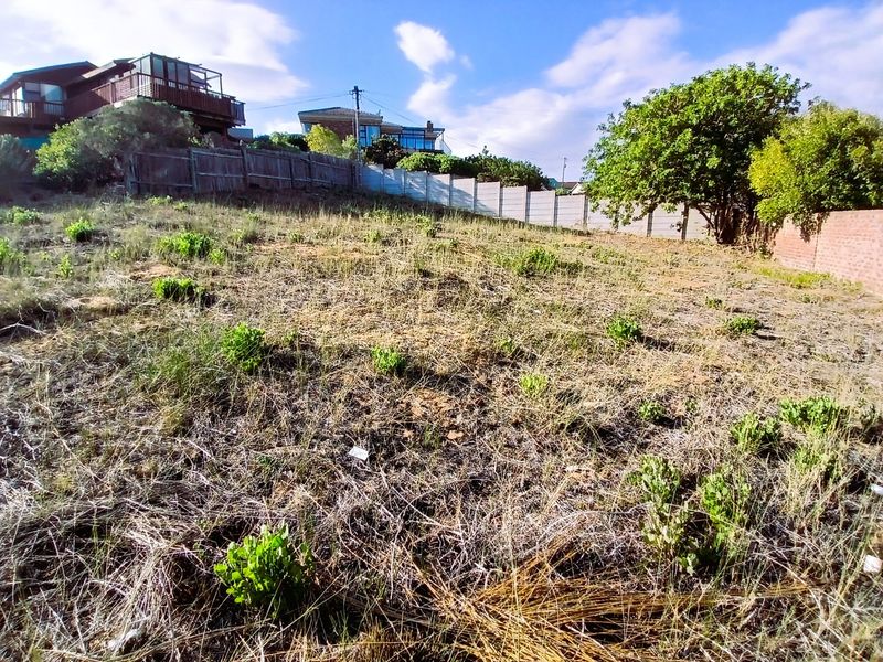 A vacant residential plot featuring a sloped landscape, enclosed by a combination of precast concrete boundary walls and timber fencing.