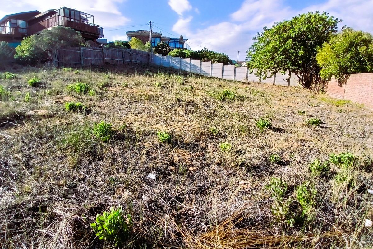 A vacant residential plot featuring a sloped landscape, enclosed by a combination of precast concrete boundary walls and timber fencing.
