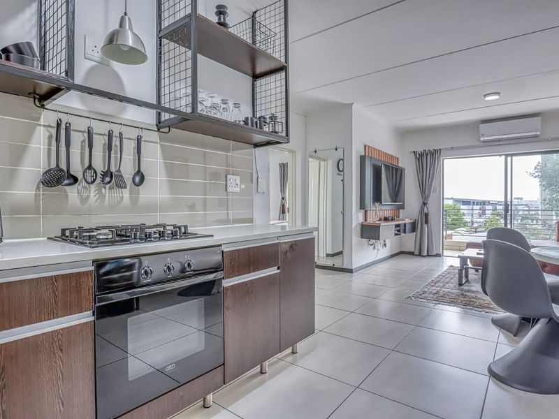 Modern open-plan living area featuring a well-equipped kitchen with built-in oven, gas hob, and tiled flooring, leading to a bright lounge with balcony access.