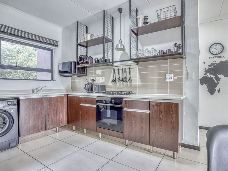 Modern kitchen featuring dark wood cabinetry, built-in oven with gas hob, tiled backsplash, open shelving, and a dedicated space for a washing machine.