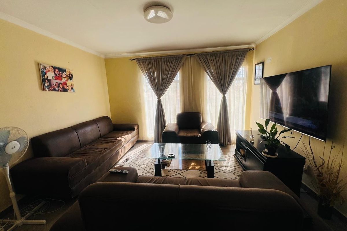 A comfortable living room featuring neutral wall tones, large windows with curtain treatments, and a central ceiling light fixture.