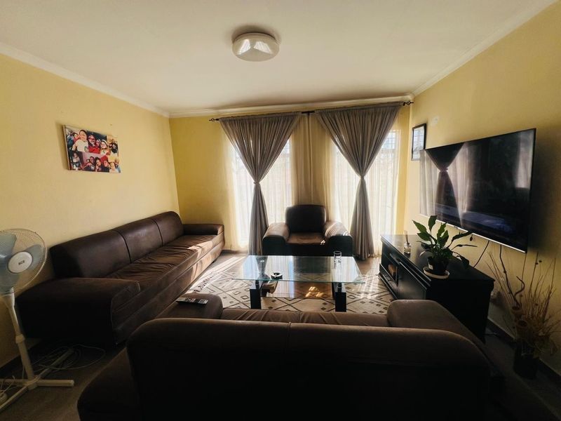 A comfortable living room featuring neutral wall tones, large windows with curtain treatments, and a central ceiling light fixture.