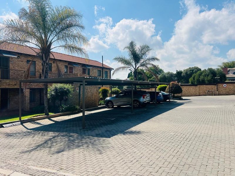 Exterior view of the apartment complex featuring a paved parking area with covered carports and established landscaping.