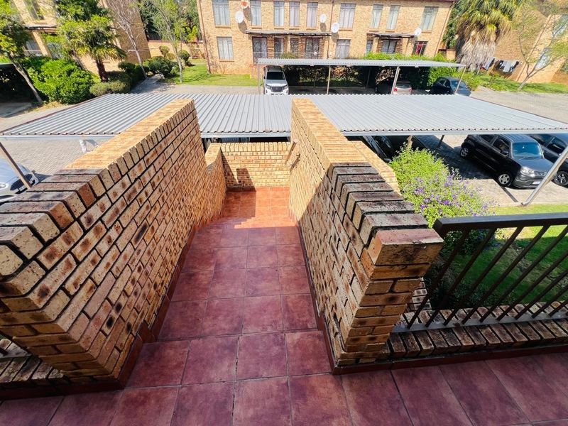 An outdoor brick staircase with tiled steps and a metal handrail, overlooking a residential complex parking area with carports.
