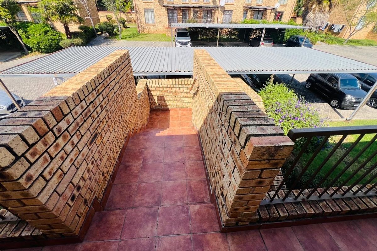 An outdoor brick staircase with tiled steps and a metal handrail, overlooking a residential complex parking area with carports.