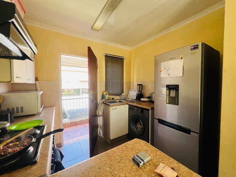 Compact kitchen featuring built-in cabinetry, laminate countertops, a stainless steel sink, and a built-in hob with an extractor fan, leading to an outdoor balcony.