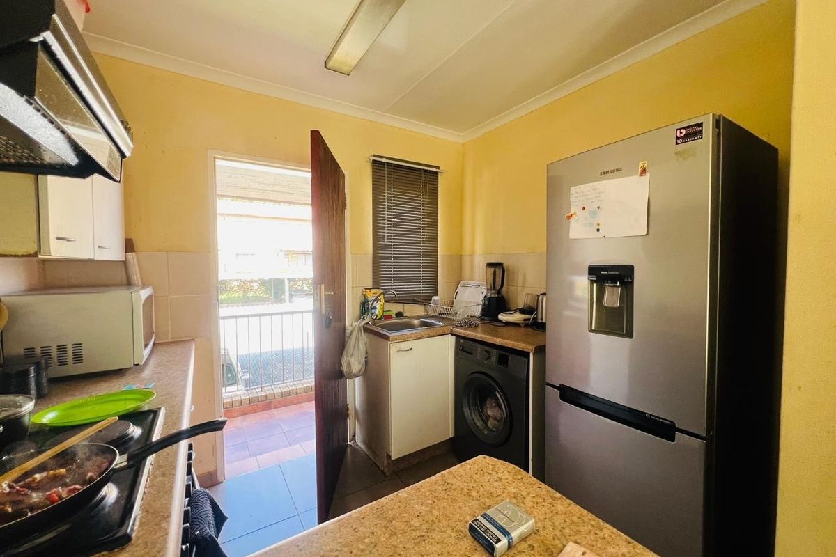 Compact kitchen featuring built-in cabinetry, laminate countertops, a stainless steel sink, and a built-in hob with an extractor fan, leading to an outdoor balcony.