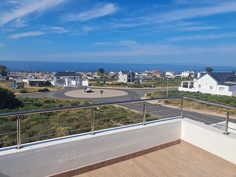 An elevated balcony featuring a modern stainless steel balustrade and tiled flooring, offering expansive views of the surrounding coastal neighborhood and ocean.