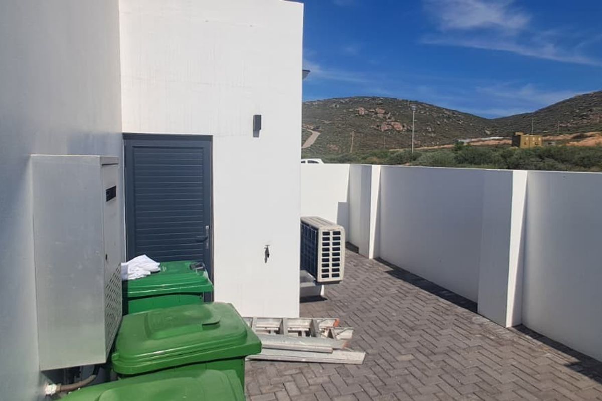 A paved rear courtyard area featuring boundary walls, an external air conditioning unit, and an outdoor tap.