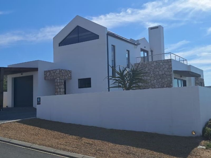 Modern architectural house featuring stone cladding, a garage, carport, and a balcony, set behind a clean white boundary wall.