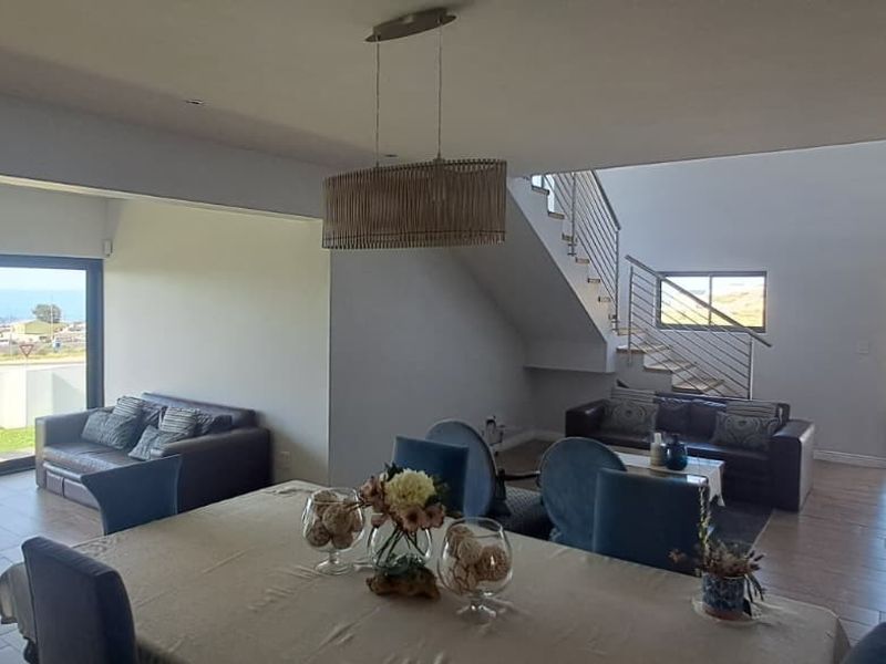 Spacious open-plan living and dining area featuring tiled floors, a modern staircase with stainless steel balustrades, and large sliding doors with ocean views.