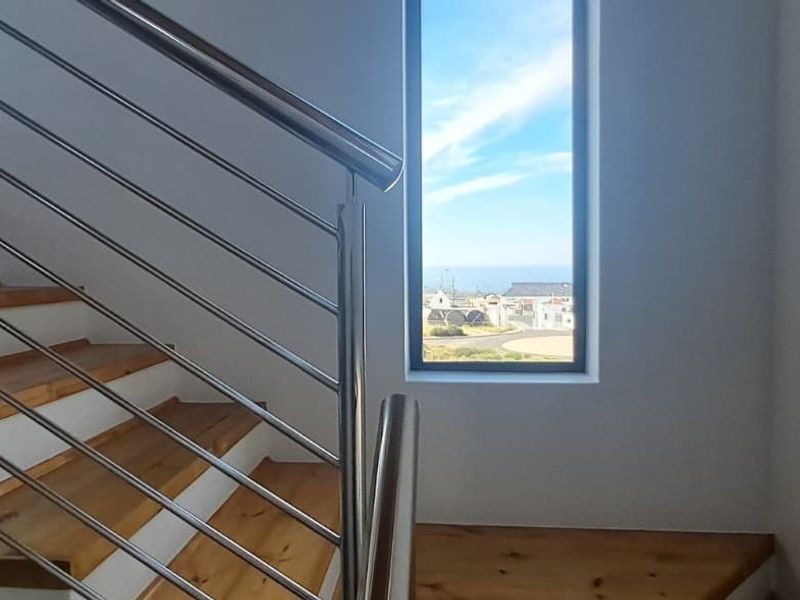 Modern staircase featuring timber treads and a sleek stainless steel balustrade, complemented by a vertical window offering natural light and exterior views.
