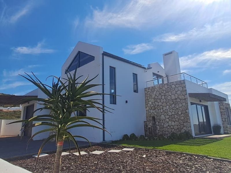 Modern architectural house exterior featuring stone cladding, a timber pergola, and a balcony, set within a well-maintained landscaped garden.
