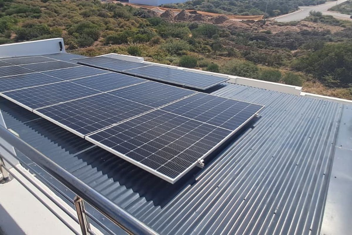 Aerial view of a corrugated metal roof featuring a modern solar panel installation and a stainless steel balcony railing.