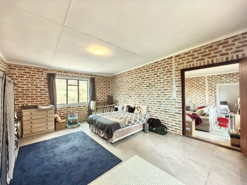 Spacious bedroom featuring rustic exposed brick walls, tiled flooring, and large windows, offering a unique character-filled living space.