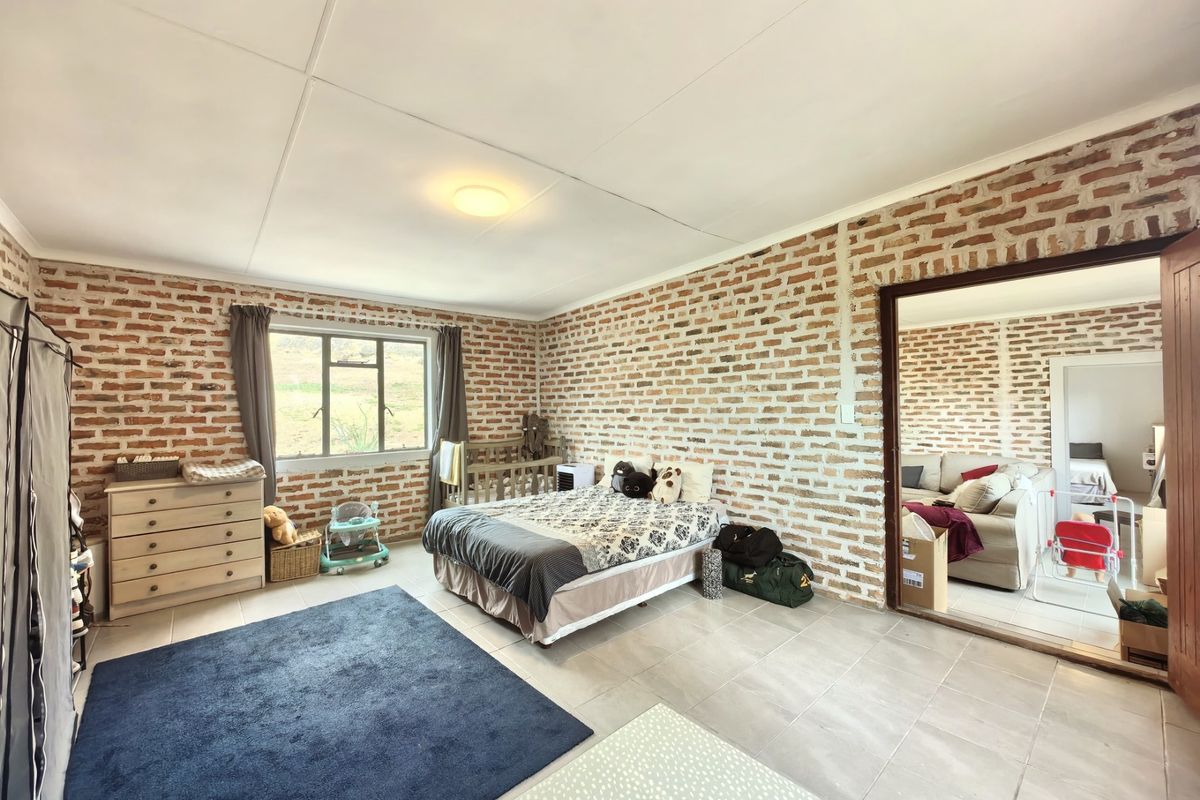 Spacious bedroom featuring rustic exposed brick walls, tiled flooring, and large windows, offering a unique character-filled living space.