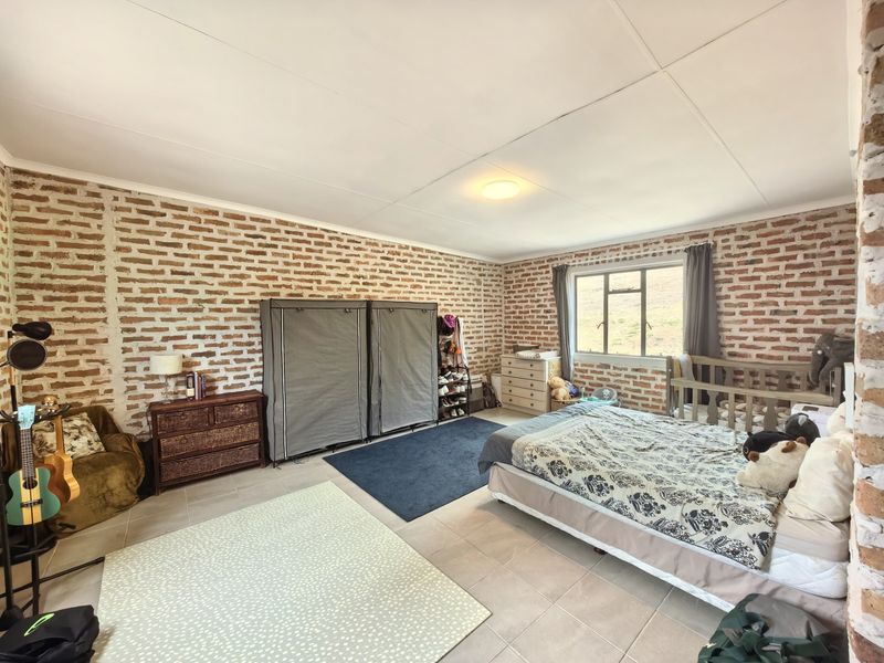 Spacious bedroom featuring rustic exposed brick walls, neutral tiled flooring, and natural light from a large window.