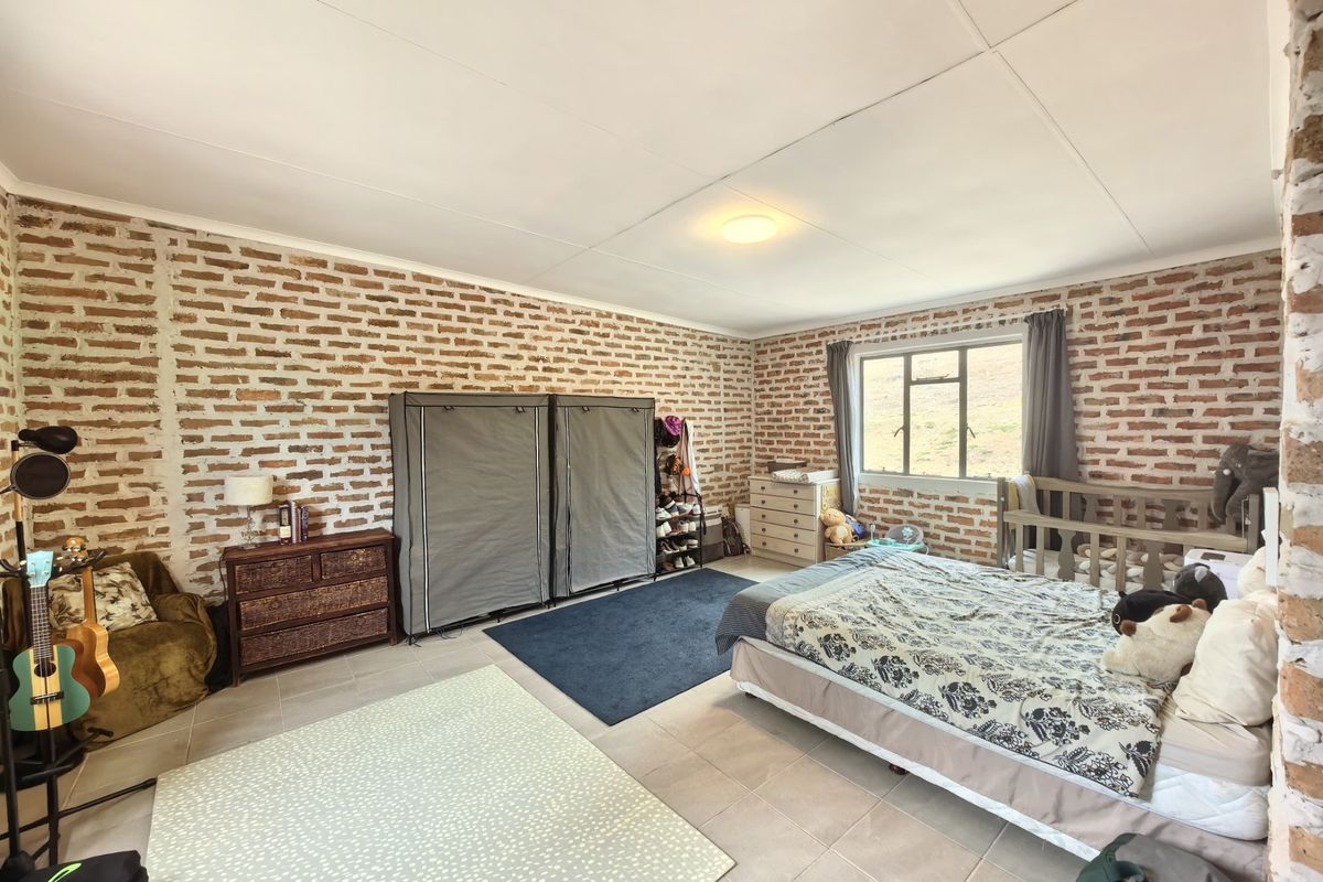 Spacious bedroom featuring rustic exposed brick walls, neutral tiled flooring, and natural light from a large window.