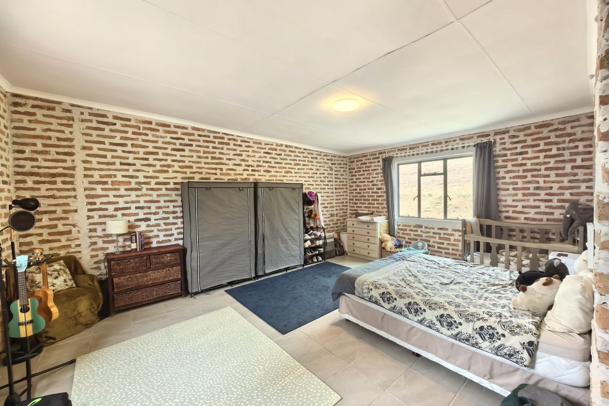 Spacious bedroom featuring exposed brick walls, tiled flooring, and natural light through an aluminium-framed window.