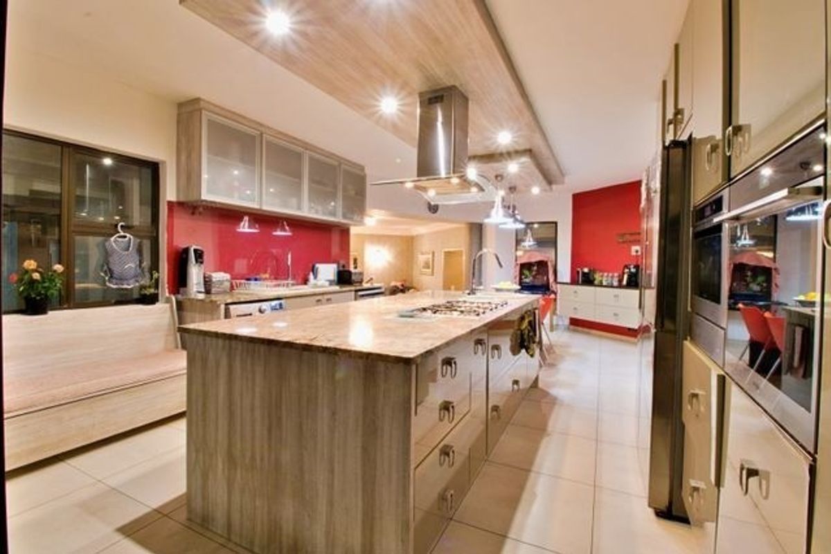 Modern kitchen featuring a large central island with granite countertops, built-in stainless steel appliances, and extensive cabinetry with integrated lighting.