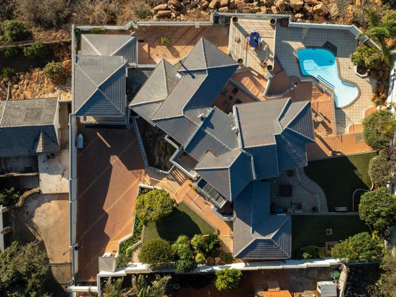 Aerial view of a residential property featuring a complex tiled roof structure, a swimming pool, paved driveway, and landscaped garden areas.