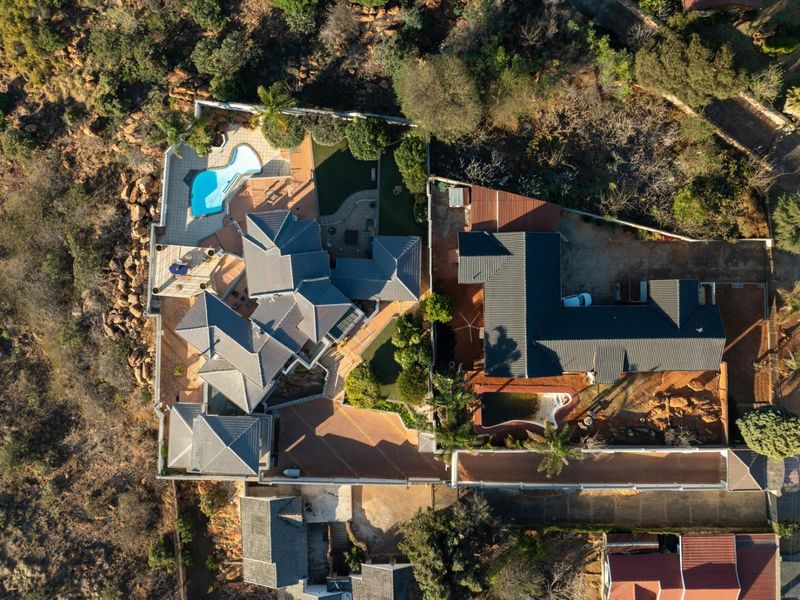 An aerial view of the property showcasing the layout, multiple roof structures, swimming pools, paved areas, and surrounding landscaped grounds.