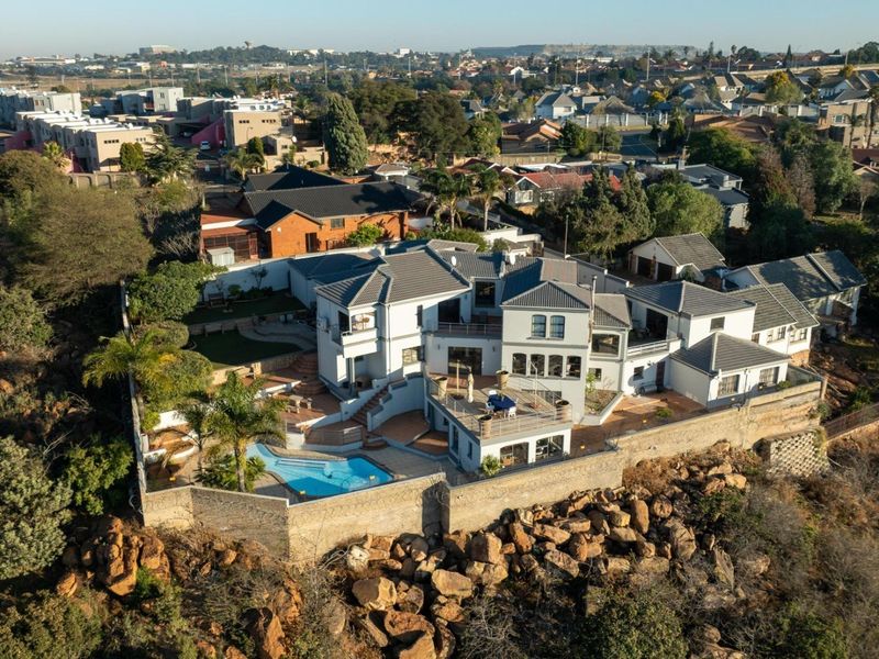 Aerial view of a large multi-level residential property featuring a swimming pool, expansive patio areas, and a secure perimeter wall.