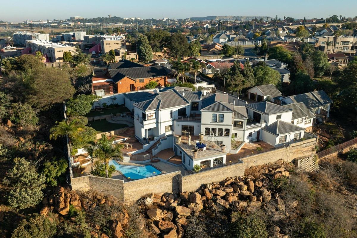 Aerial view of a large multi-level residential property featuring a swimming pool, expansive patio areas, and a secure perimeter wall.