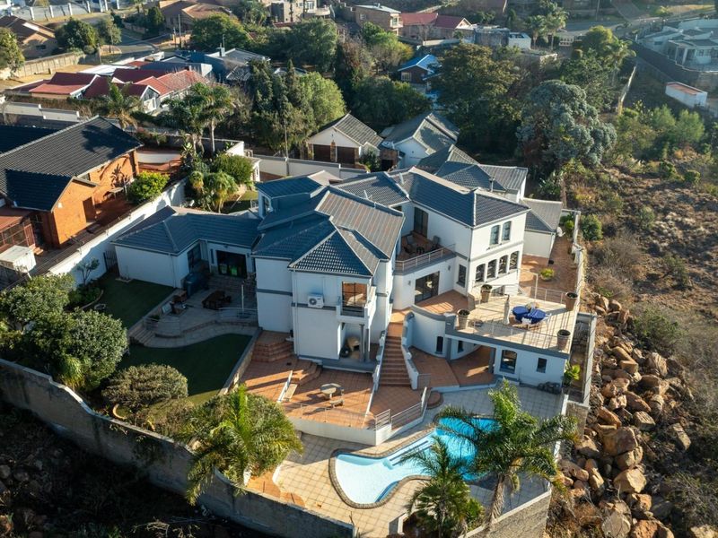 Aerial view of a multi-level residential property featuring a tiled roof, swimming pool, expansive paved patio areas, and a secure boundary wall.