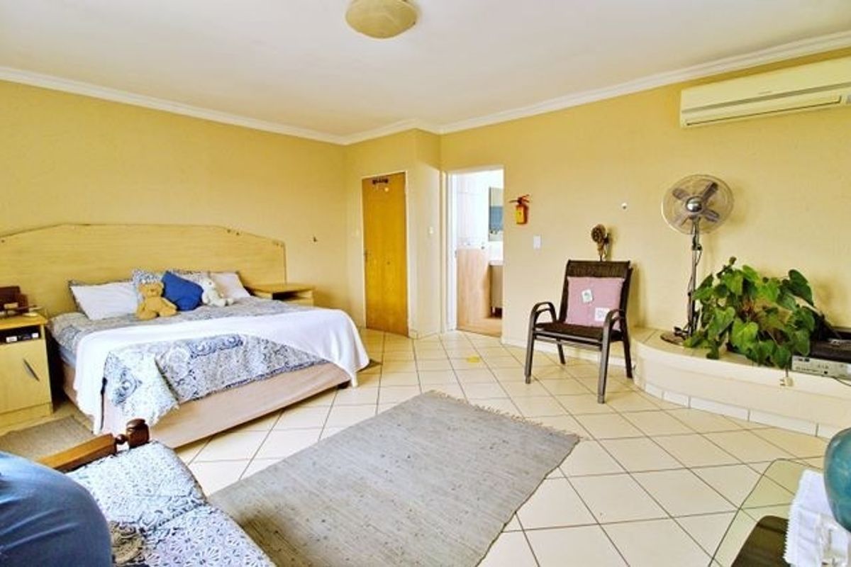 Spacious bedroom featuring tiled flooring, an integrated headboard, and a wall-mounted air conditioning unit with direct access to an en-suite bathroom.