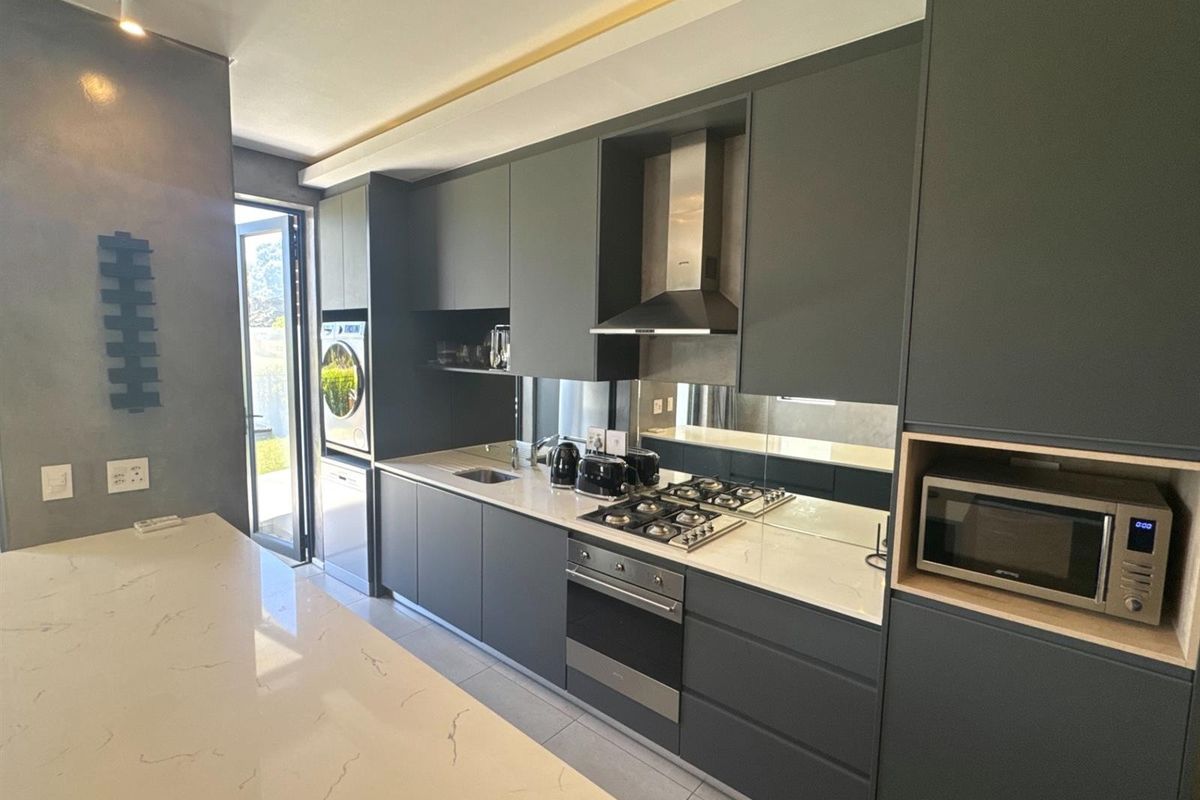 Modern kitchen featuring dark cabinetry, quartz countertops, mirrored splashback, and high-quality built-in appliances, including a gas hob and oven.