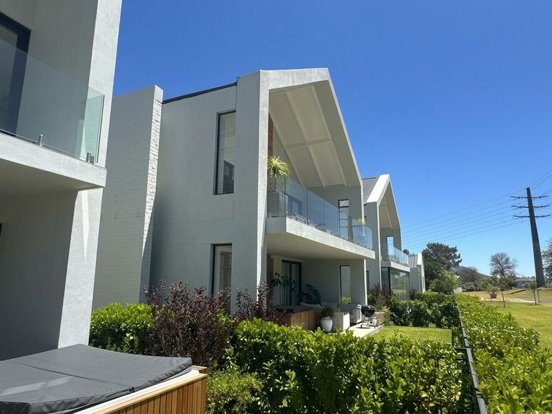 Rear view of modern apartment building featuring clean architectural lines, glass-fronted balconies, and well-maintained landscaped garden areas.