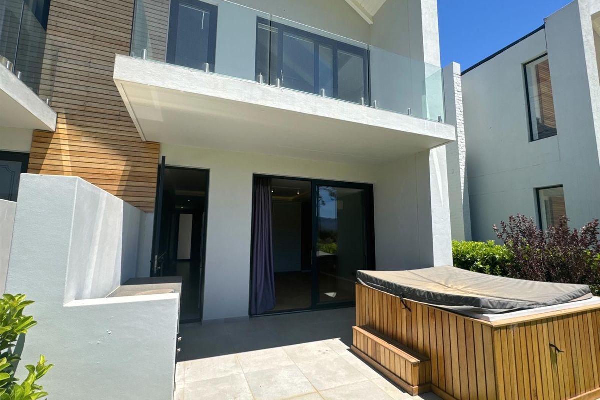 Rear view of a modern apartment featuring a tiled patio, glass balustrade balcony above, and contemporary architectural finishes.