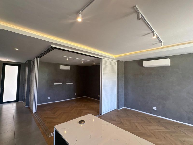Modern open-plan living area featuring herringbone timber flooring, recessed ambient lighting, split-system air conditioning, and versatile sliding partition doors for flexible space usage.