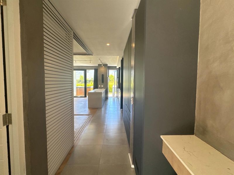 A modern, well-lit hallway featuring sleek built-in cabinetry and tiled flooring, leading towards an open-plan living area with natural light.